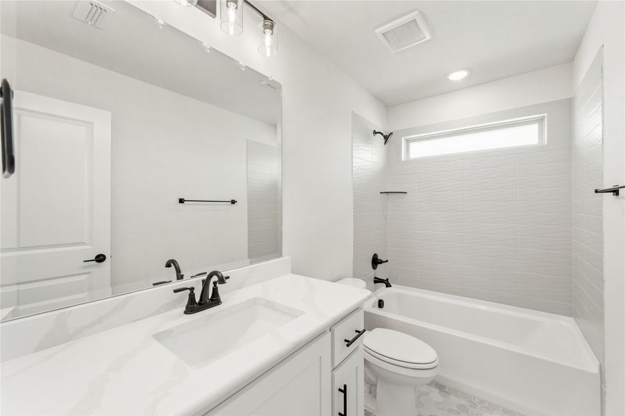 Full bathroom with white vanity, quartz countertop, tub-shower combo, and black fixtures