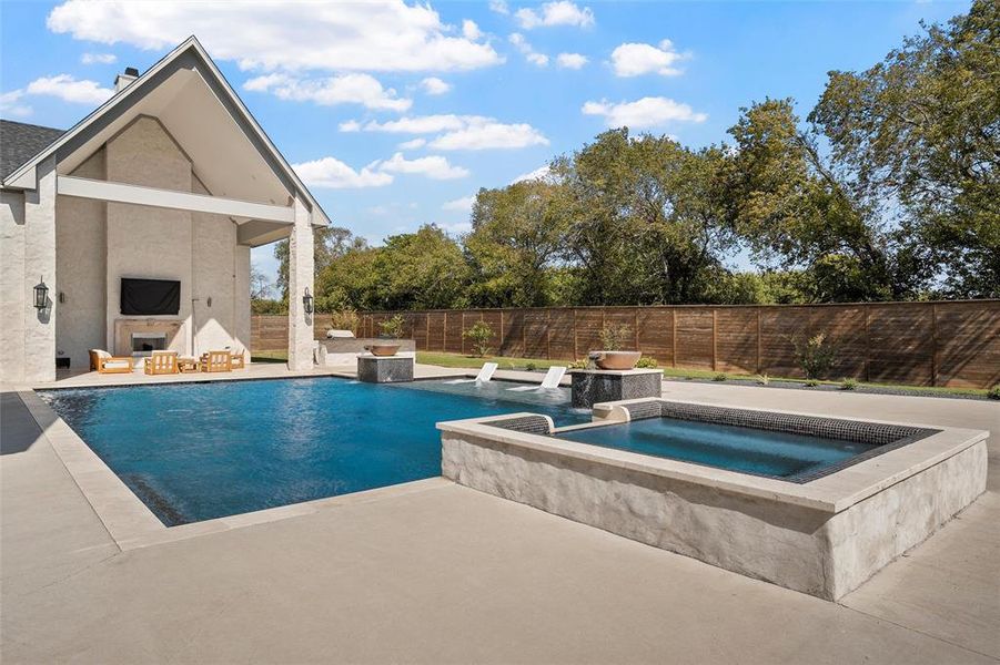 View of pool featuring a fireplace, a fenced backyard, a patio area, and a pool with connected hot tub