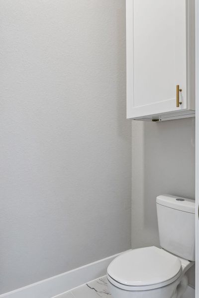 A pristine powder room with a sleek white toilet and convenient overhead cabinetry.