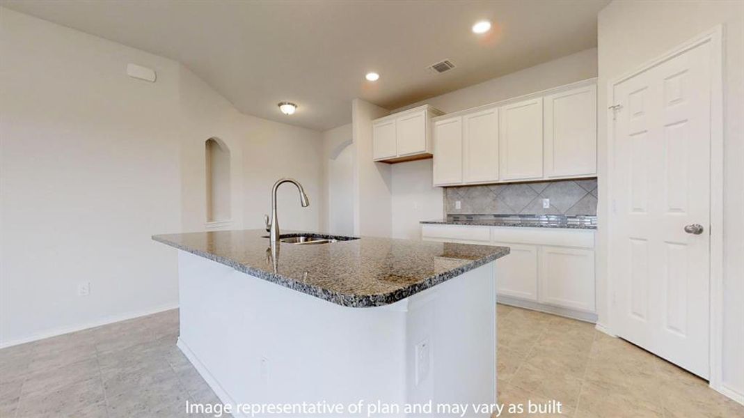 Kitchen featuring decorative backsplash, dark stone countertops, white cabinetry, an island with sink, and arched walkways Kitchen featuring decorative backsplash, dark stone countertops, white cabinetry, an island with sink, and arched walkways