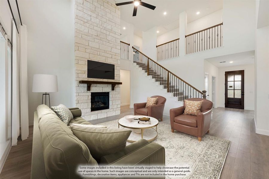 Two-story living room with stone fireplace, high ceiling, staircase, and hardwood floors