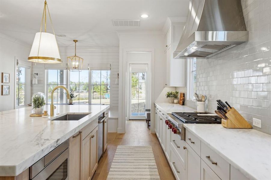 Kitchen with visible vents, decorative backsplash, stainless steel appliances, wall chimney range hood, and a sink Kitchen with visible vents, decorative backsplash, stainless steel appliances, wall chimney range hood, and a sink