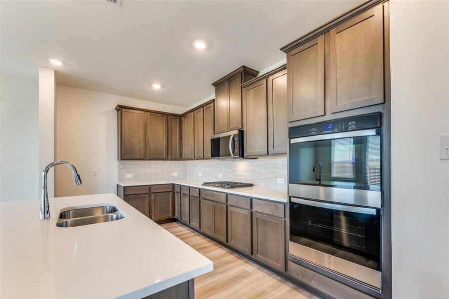 Kitchen featuring stainless steel appliances, light countertops, decorative backsplash, light wood-style flooring, and recessed lighting