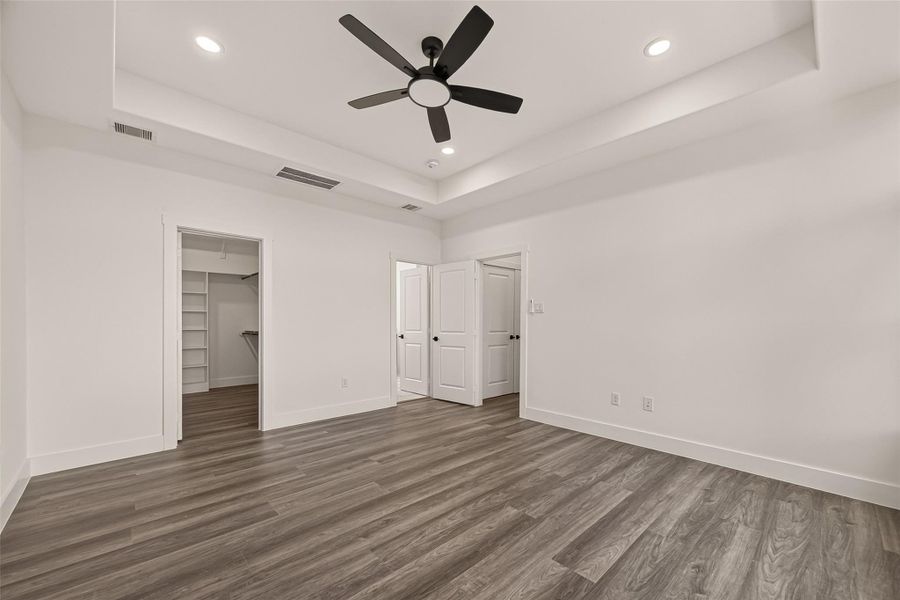 Spacious bedroom featuring modern wood flooring, recessed lighting, a ceiling fan, and a walk-in closet. The room has a clean, minimalist design with neutral walls and white trim. Spacious bedroom featuring modern wood flooring, recessed lighting, a ceiling fan, and a walk-in closet. The room has a clean, minimalist design with neutral walls and white trim.