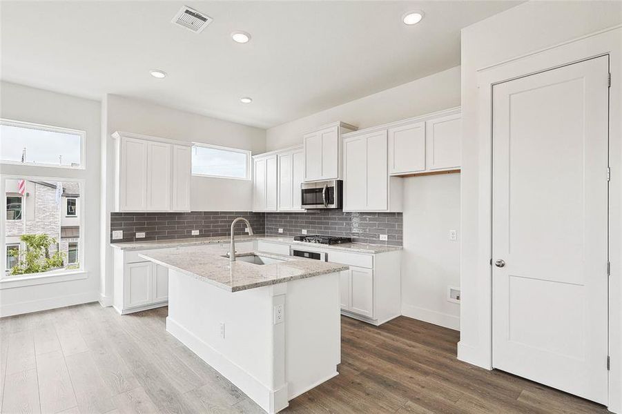 Kitchen featuring white cabinetry, hardwood / wood-style flooring, decorative backsplash, sink, and a kitchen island with sink