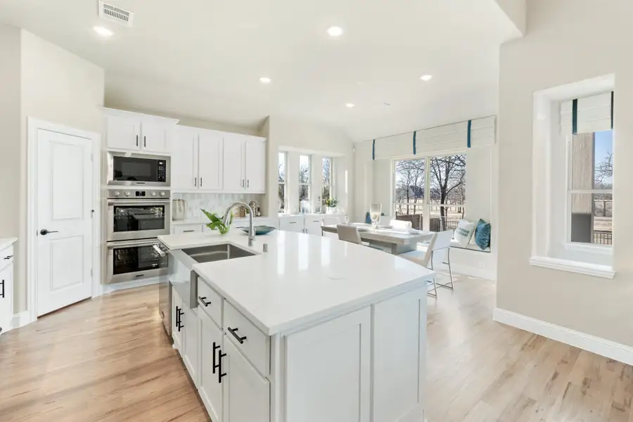 Open kitchen with white cabinets, large island, stainless steel appliances, and hardwood floors opening to a dining area. Open kitchen with white cabinets, large island, stainless steel appliances, and hardwood floors opening to a dining area.