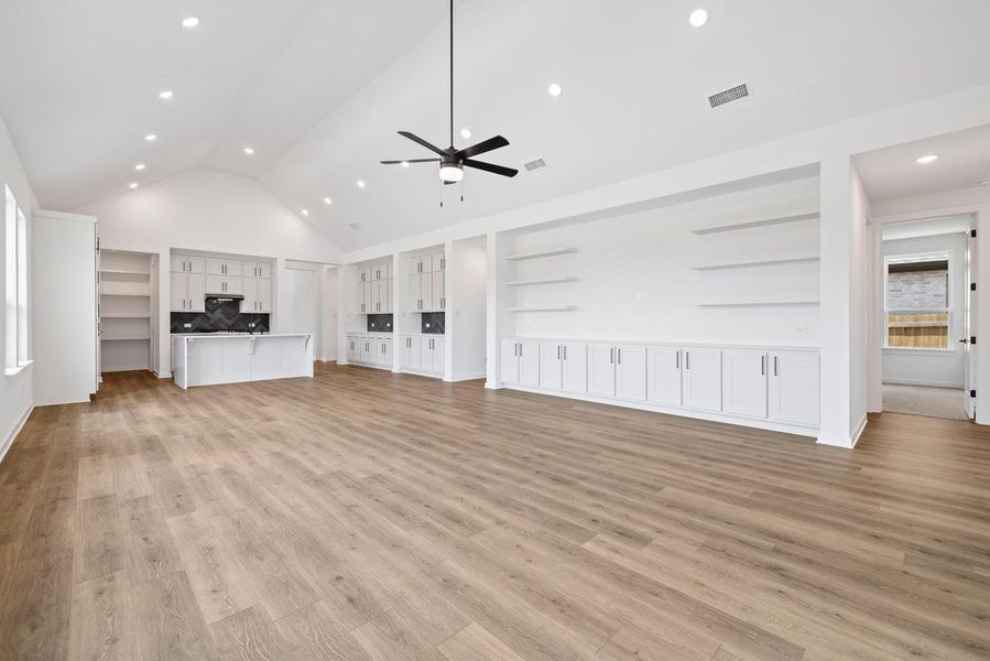 Unfurnished living room featuring a ceiling fan, light wood-style floors, built in features, high vaulted ceiling, and recessed lighting Unfurnished living room featuring a ceiling fan, light wood-style floors, built in features, high vaulted ceiling, and recessed lighting