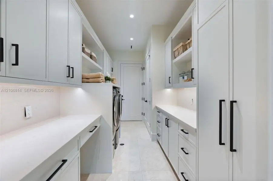 Custom cabinetry with matte black hardware, stone countertops, integrated under-cabinet lighting, and light-toned tile flooring Custom cabinetry with matte black hardware, stone countertops, integrated under-cabinet lighting, and light-toned tile flooring