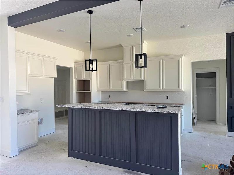 Kitchen with a kitchen island, white cabinets, visible vents, and unfinished concrete floors