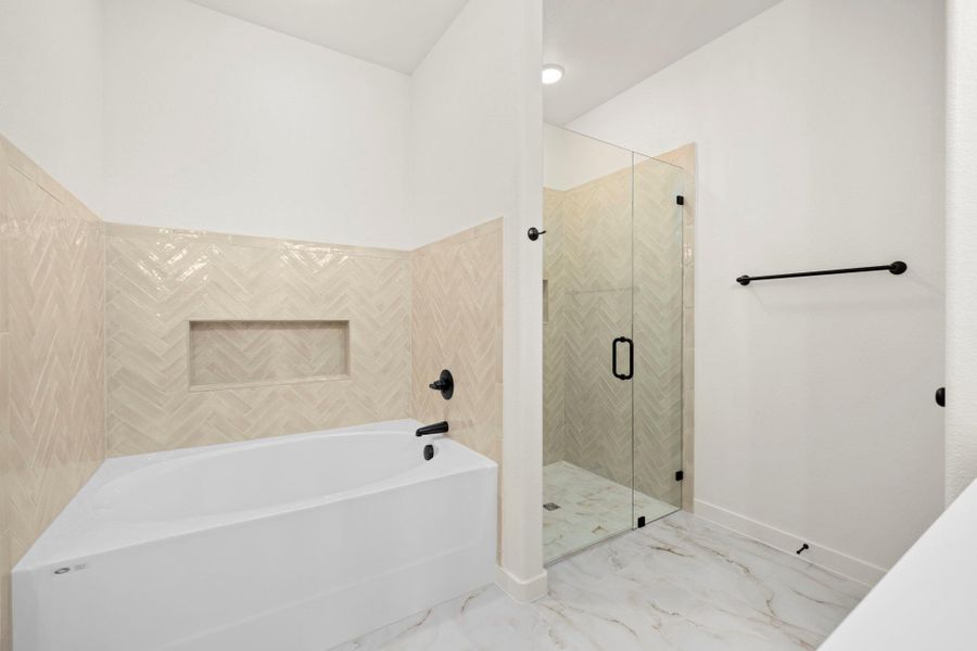 Luxurious bath features an oversized tub and a frameless glass-enclosed shower with sophisticated tile.