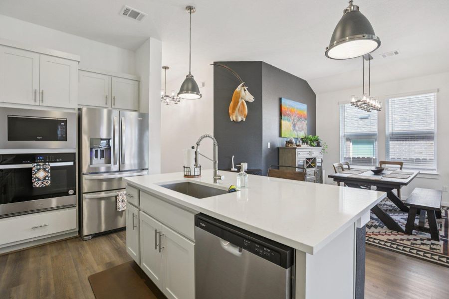 Kitchen with a chandelier, white cabinets, appliances with stainless steel finishes, hanging light fixtures, and dark wood finished floors Kitchen with a chandelier, white cabinets, appliances with stainless steel finishes, hanging light fixtures, and dark wood finished floors