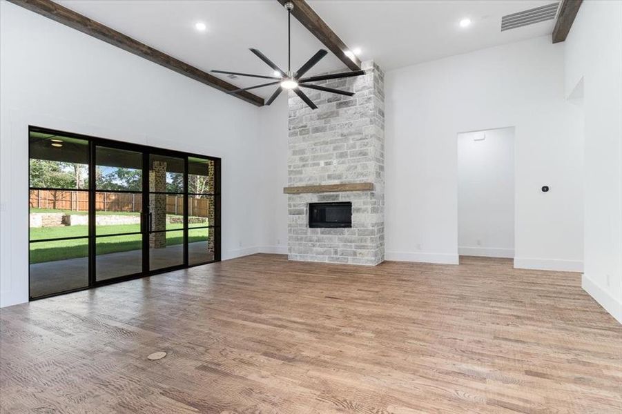 Unfurnished living room featuring light hardwood / wood-style flooring, a fireplace, ceiling fan, high vaulted ceiling, and beamed ceiling