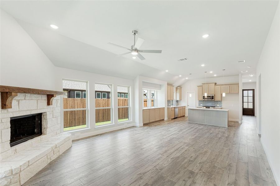 Open living area with stone fireplace, vaulted ceiling, and kitchen with light wood cabinets and island Open living area with stone fireplace, vaulted ceiling, and kitchen with light wood cabinets and island