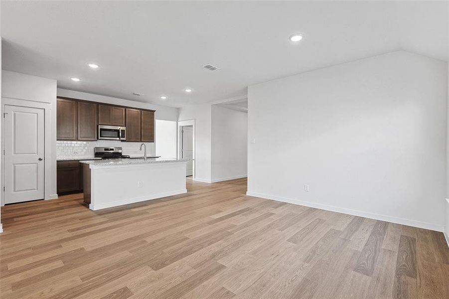 Kitchen with light wood-type flooring, appliances with stainless steel finishes, and a kitchen island with sink