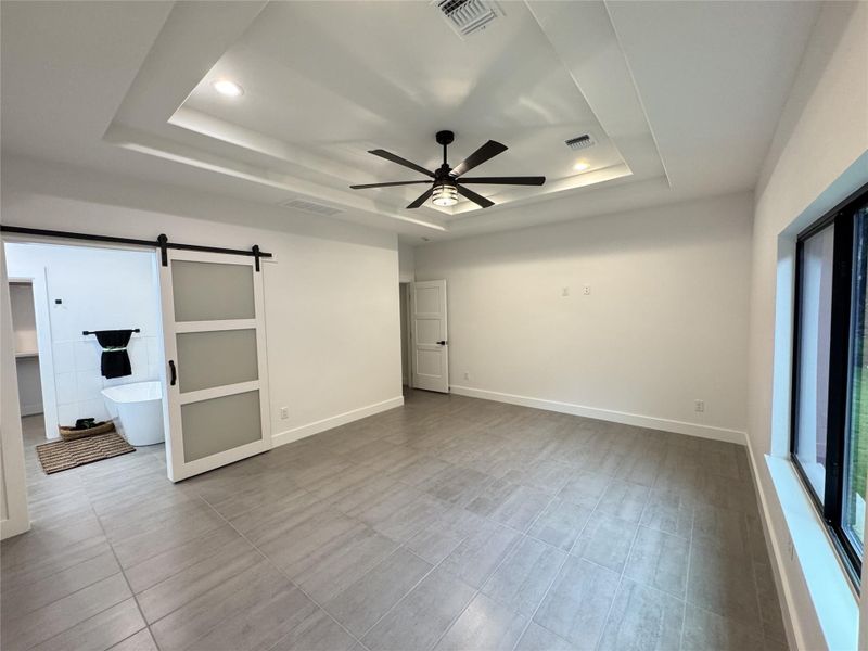Unfurnished room with a tray ceiling, a barn door, a ceiling fan, and recessed lighting Unfurnished room with a tray ceiling, a barn door, a ceiling fan, and recessed lighting