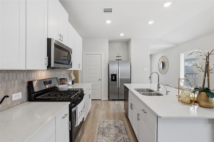 Modern kitchen with sleek white cabinetry, stainless steel appliances, and a stylish hexagonal tile backsplash. Features a spacious island with a double sink and elegant finishes. Bright and airy with natural light.