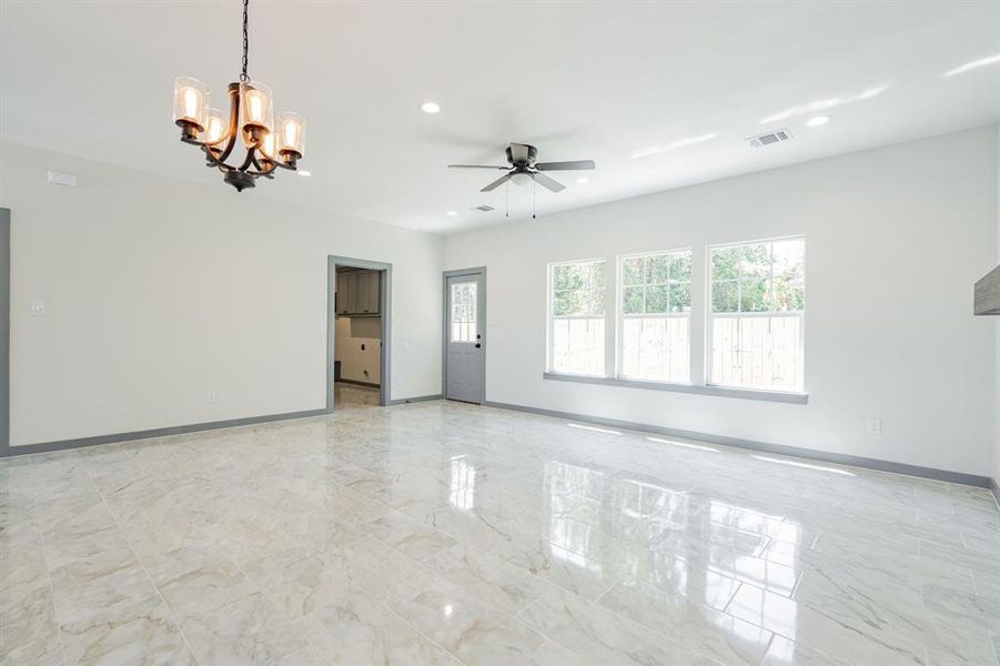 Tiled spare room featuring ceiling fan with notable chandelier