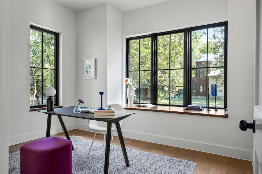 A quiet office space offers ample natural light through multiple paneled windows overlooking mature trees.