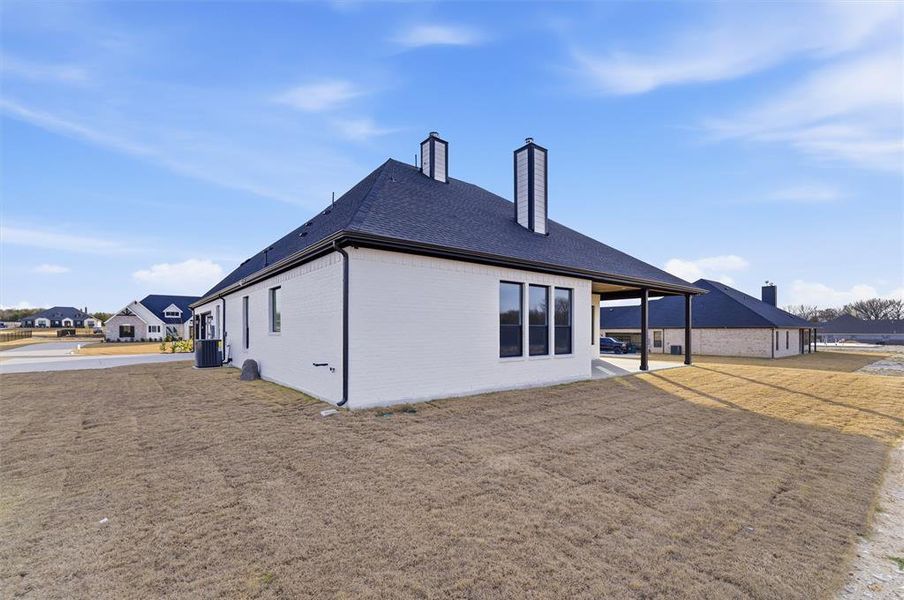 Back of property with brick siding, a chimney, a yard, a patio, and a shingled roof