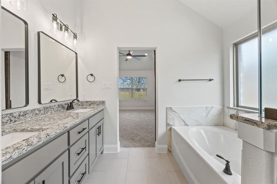 Bathroom featuring a bath, double vanity, vaulted ceiling, and light tile patterned flooring Bathroom featuring a bath, double vanity, vaulted ceiling, and light tile patterned flooring