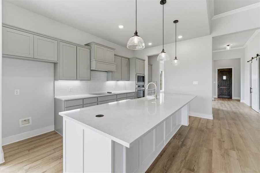 Kitchen featuring a barn door, a kitchen island with sink, light wood-style floors, hanging light fixtures, and decorative backsplash