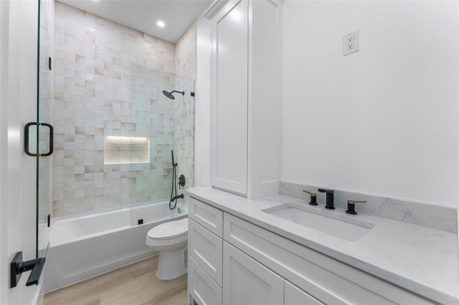 Full bath featuring vanity, light wood-style floors, and combined bath / shower with glass door