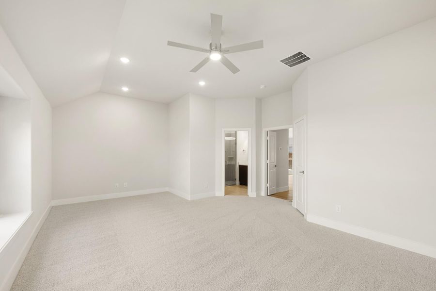 Empty bedroom with vaulted ceiling, ceiling fan, carpet flooring, and open doors to bathroom and closet