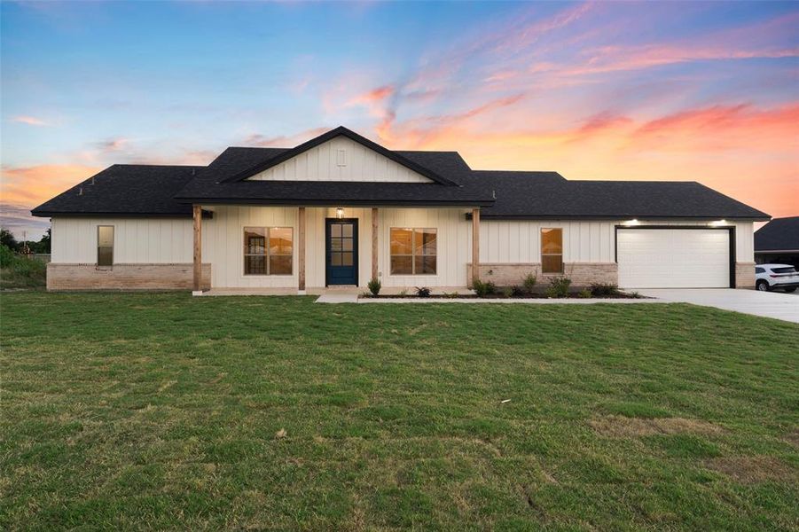 Modern farmhouse exterior featuring a dark asphalt shingle roof, white board-and-batten siding, and a stone-clad foundation Modern farmhouse exterior featuring a dark asphalt shingle roof, white board-and-batten siding, and a stone-clad foundation