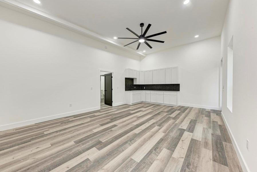 Unfurnished living room featuring ceiling fan, light wood finished floors, recessed lighting, and a high ceiling