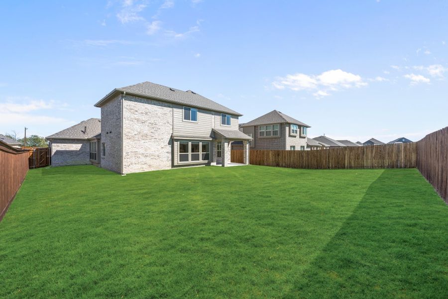 Two-story brick home with large grassy backyard enclosed by wood privacy fence