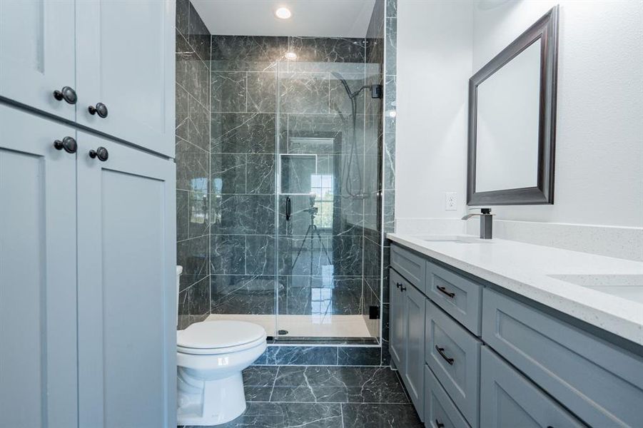 Bathroom featuring dual vanity, toilet, an enclosed shower, and tile patterned flooring