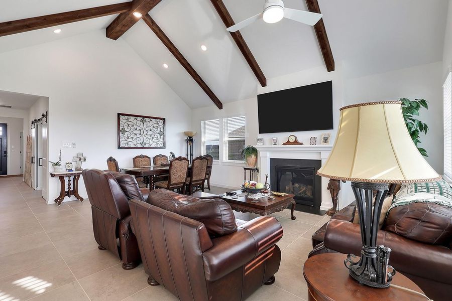 This spacious living room features a high vaulted ceiling with exposed wooden beams, a cozy fireplace. Great for entertaining with this beautiful open space! Very warm and inviting atmosphere.