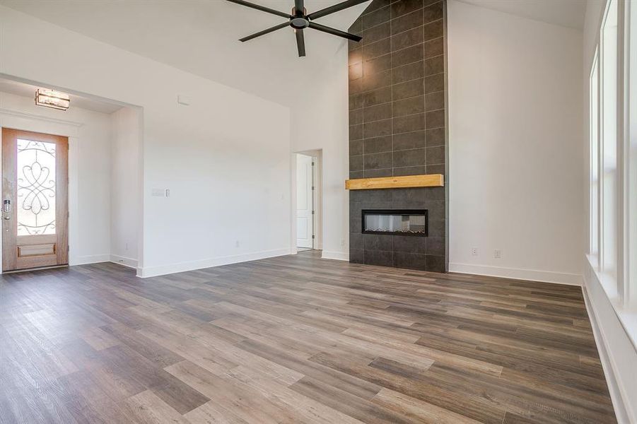 Unfurnished living room featuring lofted ceiling, ceiling fan, a tiled fireplace, and dark wood-style floors Unfurnished living room featuring lofted ceiling, ceiling fan, a tiled fireplace, and dark wood-style floors