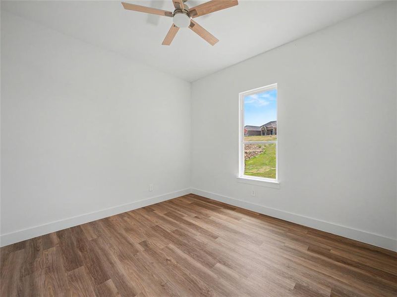 Room featuring wood-finish flooring, a single window, white walls, and a ceiling fan