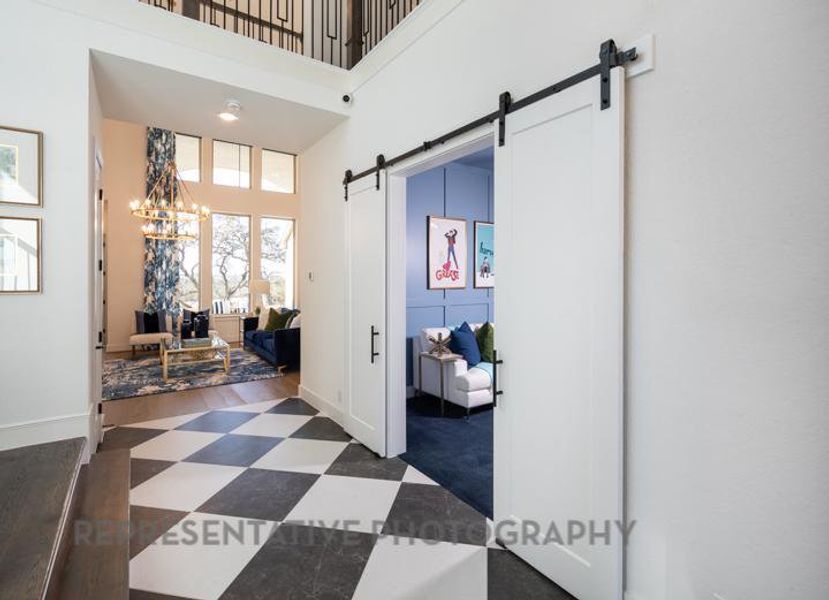 Corridor with a notable chandelier, a barn door, baseboards, tile patterned floors, and a towering ceiling Corridor with a notable chandelier, a barn door, baseboards, tile patterned floors, and a towering ceiling