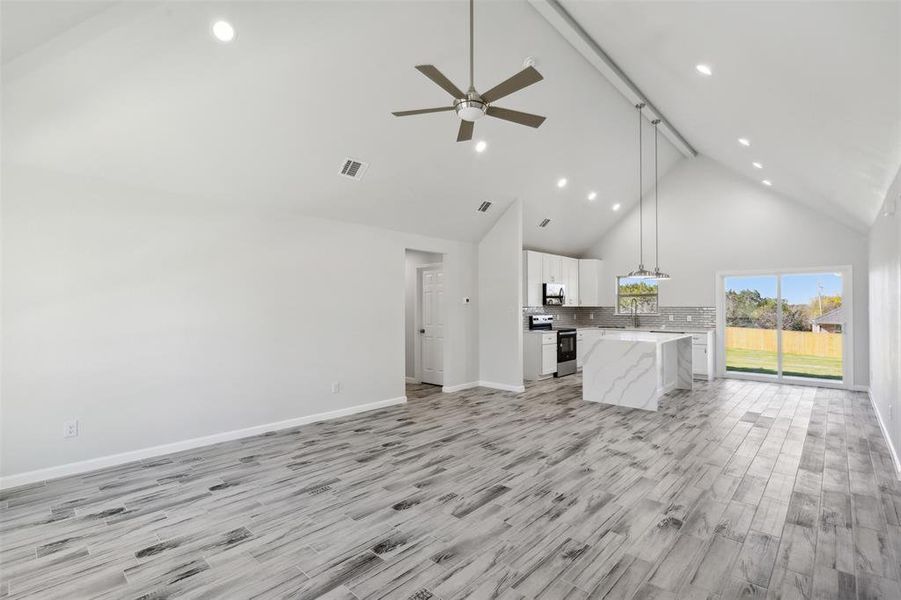 Unfurnished living room with beam ceiling, high vaulted ceiling, light hardwood / wood-style flooring, and ceiling fan