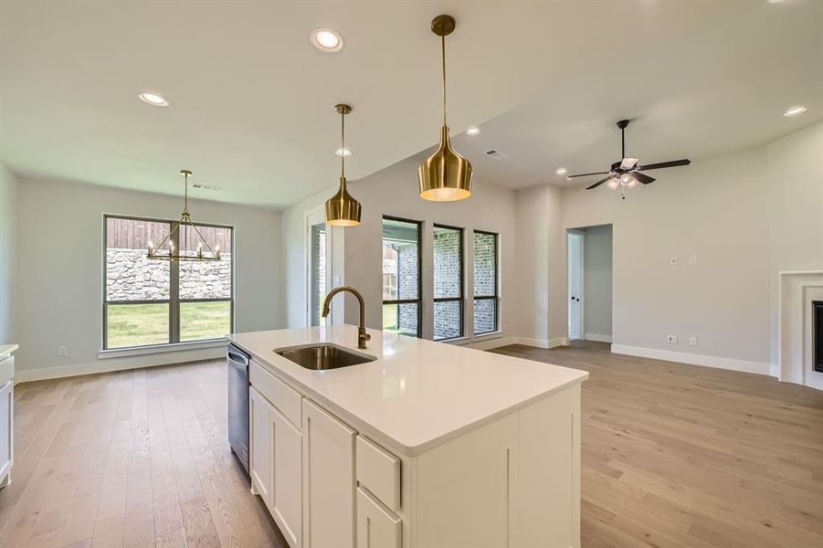 Kitchen with a chandelier, light wood finished floors, white cabinetry, light countertops, and a center island with sink Kitchen with a chandelier, light wood finished floors, white cabinetry, light countertops, and a center island with sink