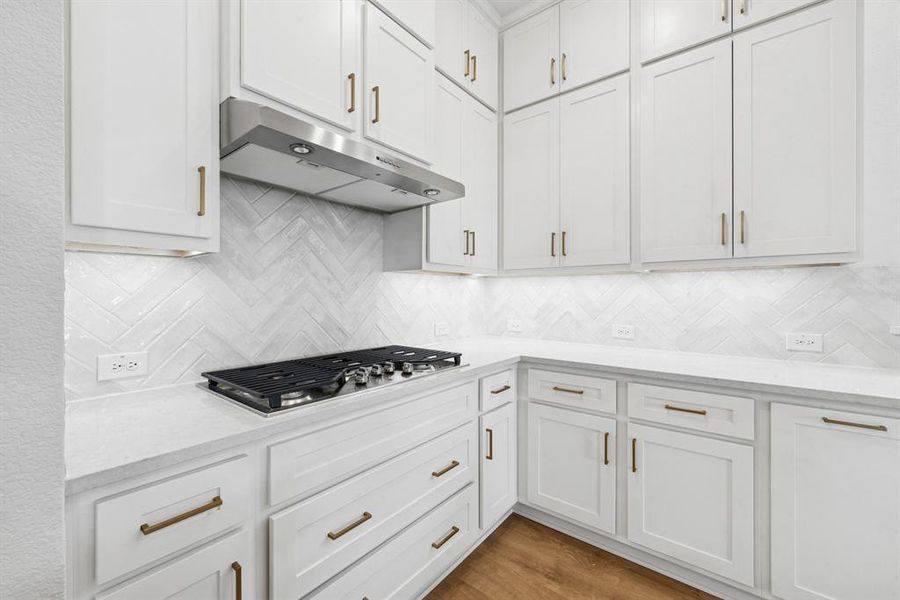Kitchen with white cabinetry, light stone countertops, light wood-style floors, and stainless steel gas stovetop Kitchen with white cabinetry, light stone countertops, light wood-style floors, and stainless steel gas stovetop