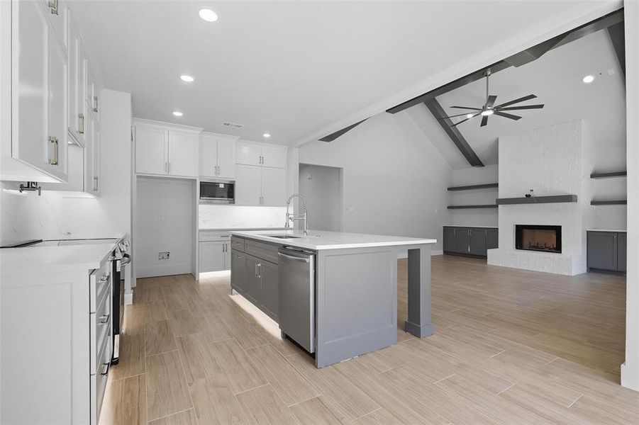 Kitchen with a center island with sink, recessed lighting, open floor plan, wood tiled floors, and a brick fireplace Kitchen with a center island with sink, recessed lighting, open floor plan, wood tiled floors, and a brick fireplace