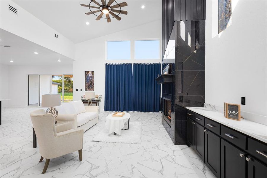 Living room with recessed lighting, high vaulted ceiling, a premium fireplace, light marble finish flooring, and a ceiling fan