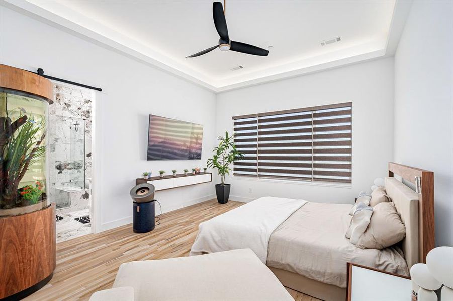 Bedroom featuring a raised ceiling, ensuite bathroom, ceiling fan, and light hardwood / wood-style floors