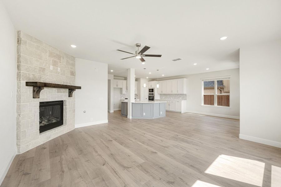 Open living area with stone fireplace, wood floors, and kitchen with island visible in background