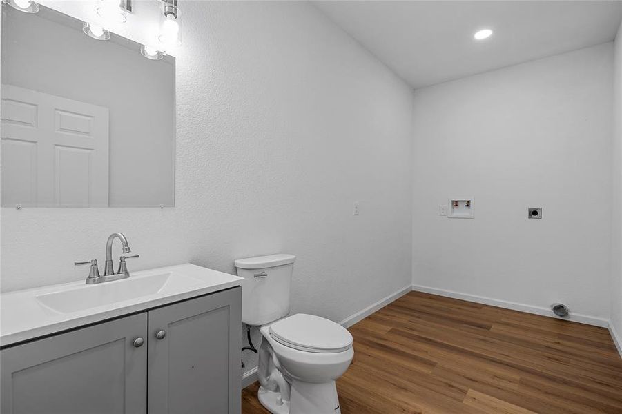 Light-filled utility room featuring wood-finish flooring, a contemporary vanity with an integrated sink, a sleek toilet, and dedicated laundry connections Light-filled utility room featuring wood-finish flooring, a contemporary vanity with an integrated sink, a sleek toilet, and dedicated laundry connections