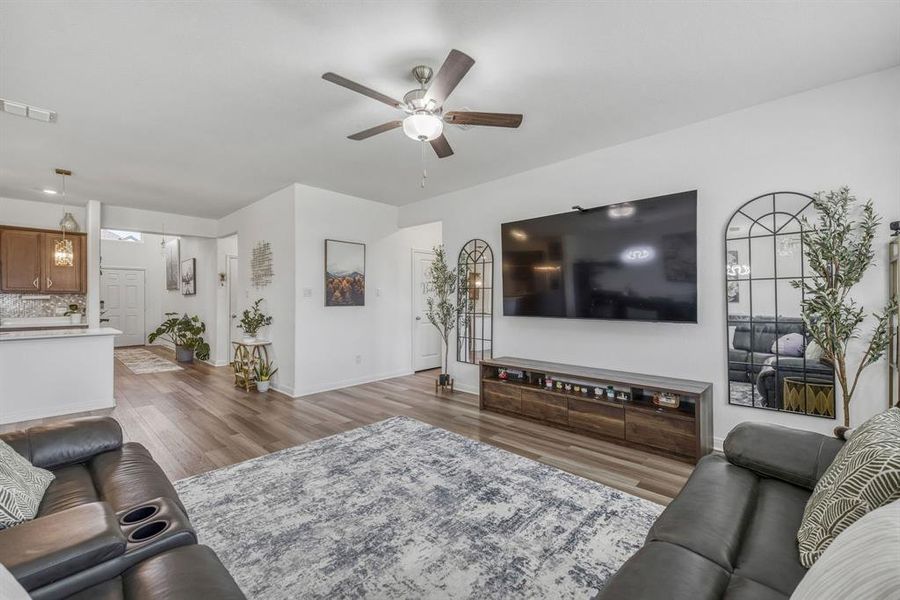 Spacious living area featuring wood-finish flooring, white walls, and a ceiling fan with integrated lighting Spacious living area featuring wood-finish flooring, white walls, and a ceiling fan with integrated lighting
