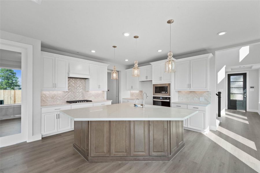 The stunning and generously sized center island features a breakfast bar, perfect for casual dining and entertaining. The island is beautifully designed with warm wood cabinetry, pristine white quartz countertop, and elegant pendant lights.