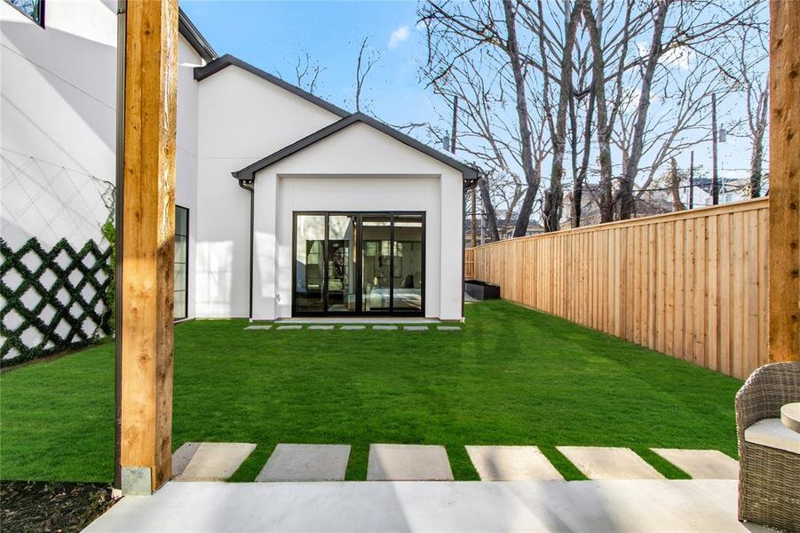 Rear exterior featuring a manicured lawn, modern white siding with black trim, a sliding glass door, privacy fencing, and concrete stepping stones