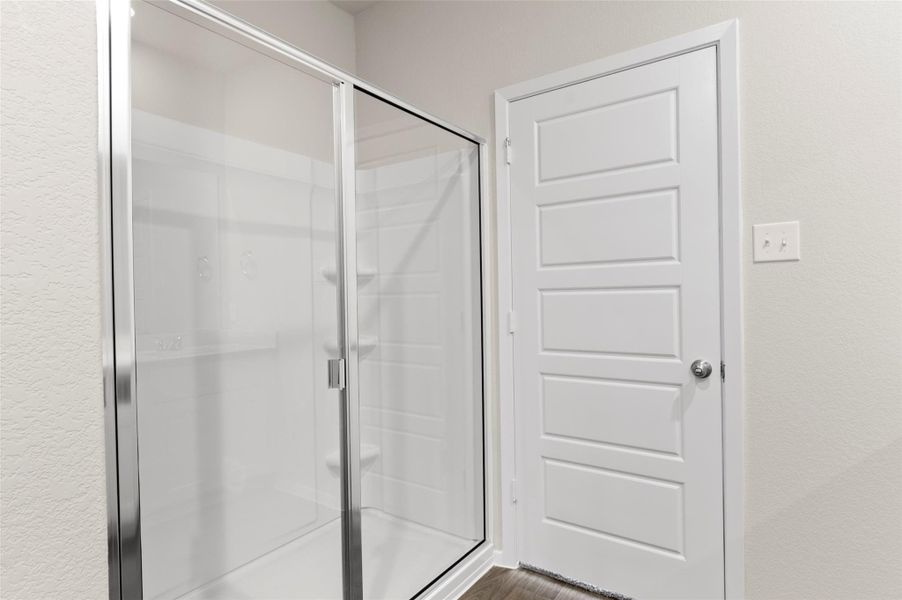 Bathroom featuring a textured wall, a stall shower, and wood finished floors Bathroom featuring a textured wall, a stall shower, and wood finished floors