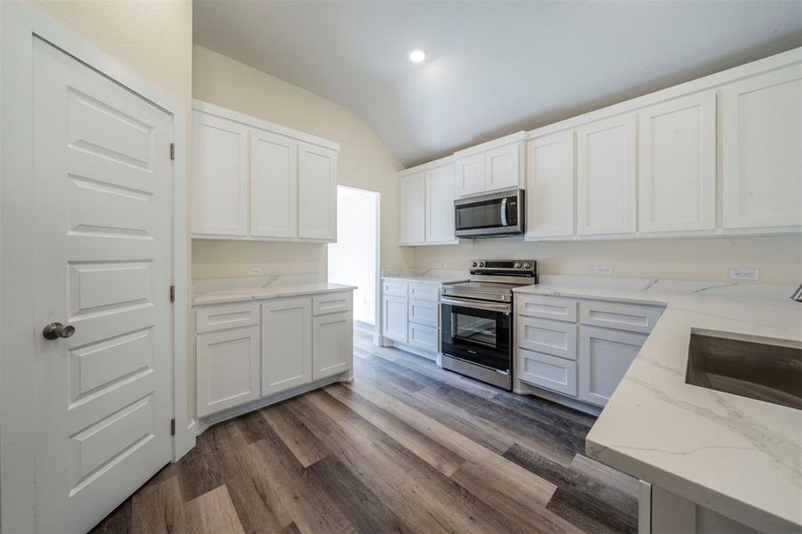 Kitchen featuring stainless steel appliances, dark wood-type flooring, white cabinetry, vaulted ceiling, and light stone countertops