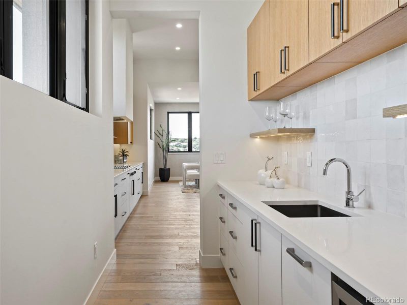 Butler's pantry with sink, beverage cooler and additional storage.  Across from walk-in pantry.