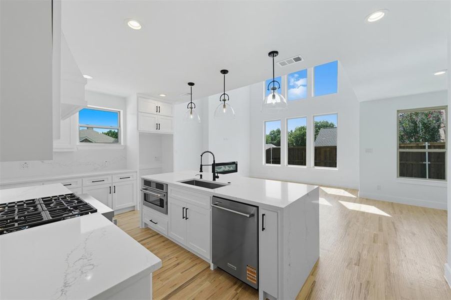 Kitchen with light stone counters, a kitchen island with sink, light wood-style flooring, white cabinetry, and stainless steel appliances